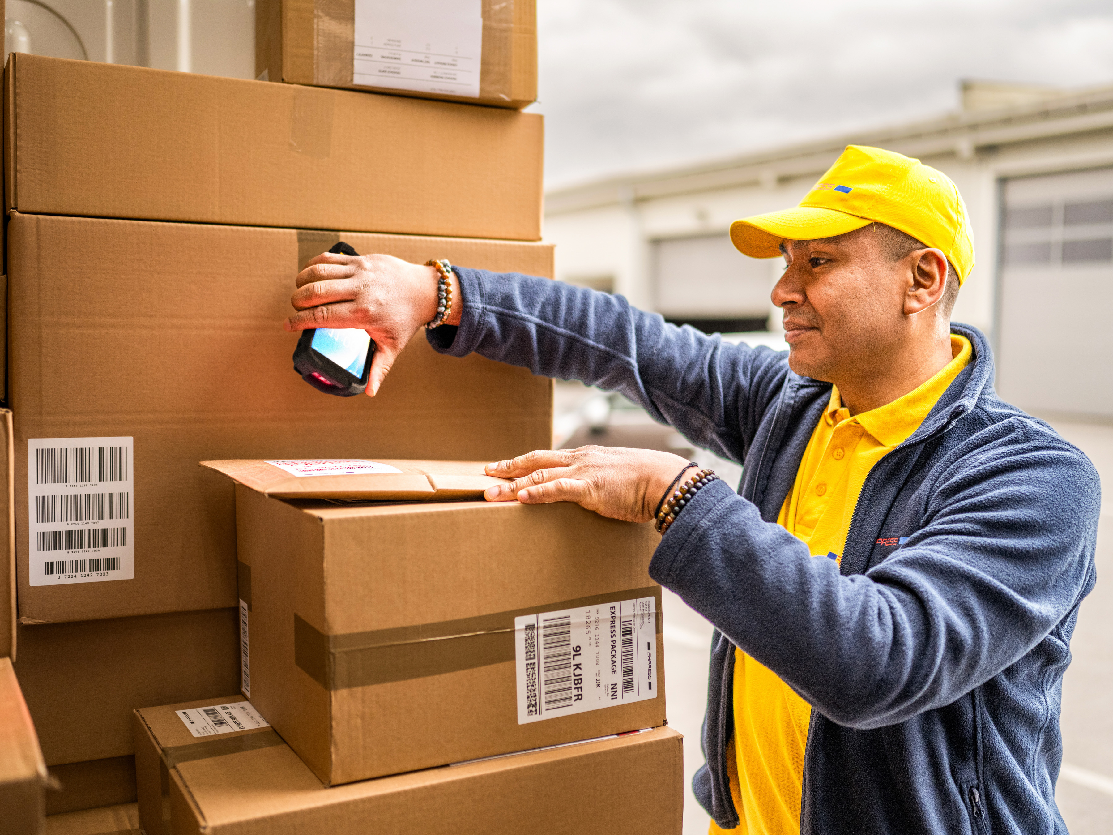 A transportation and logistics worker using a handheld mobile computer to scan packages inside the back of a delivery truck.