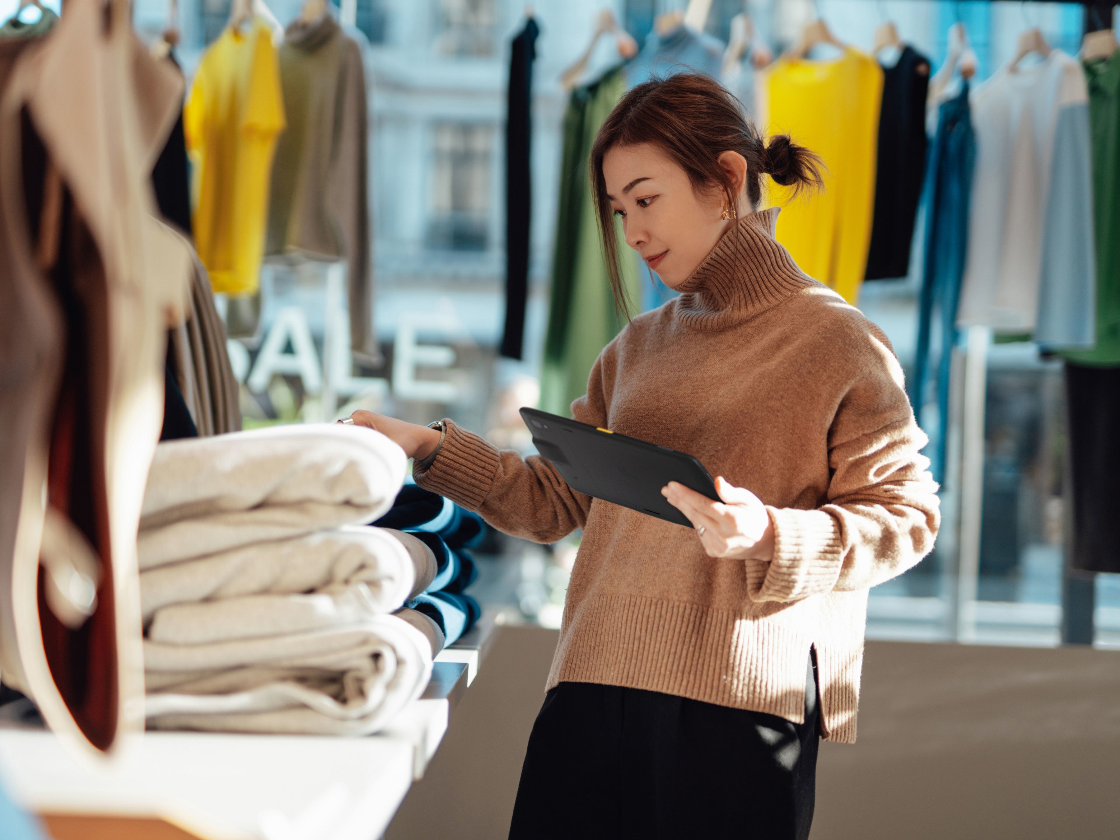 A retail employee using a tablet to check stock inside of a  clothing store.