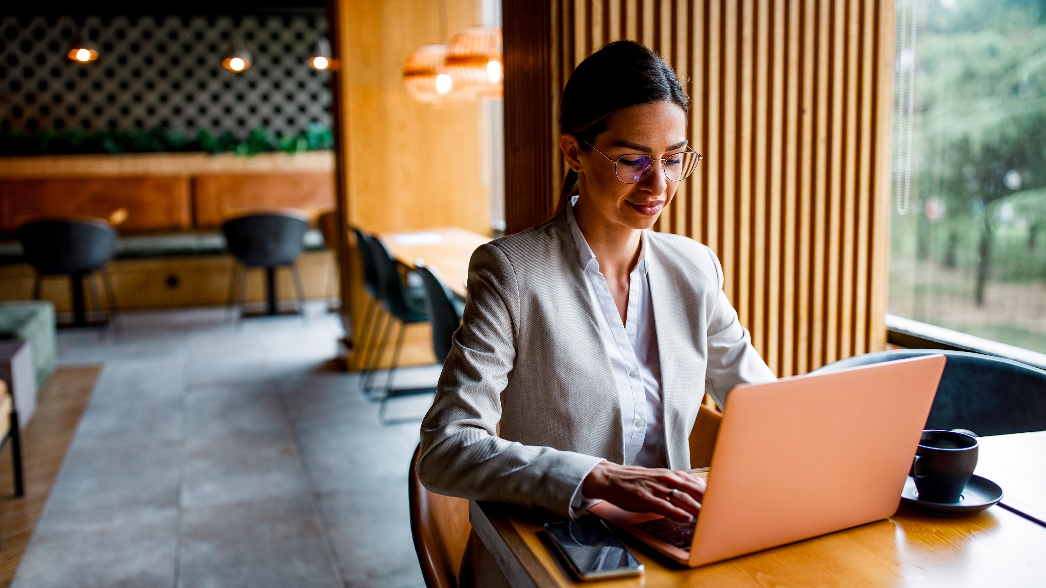 An employee is working remotely on a laptop at a wooden table in a café.