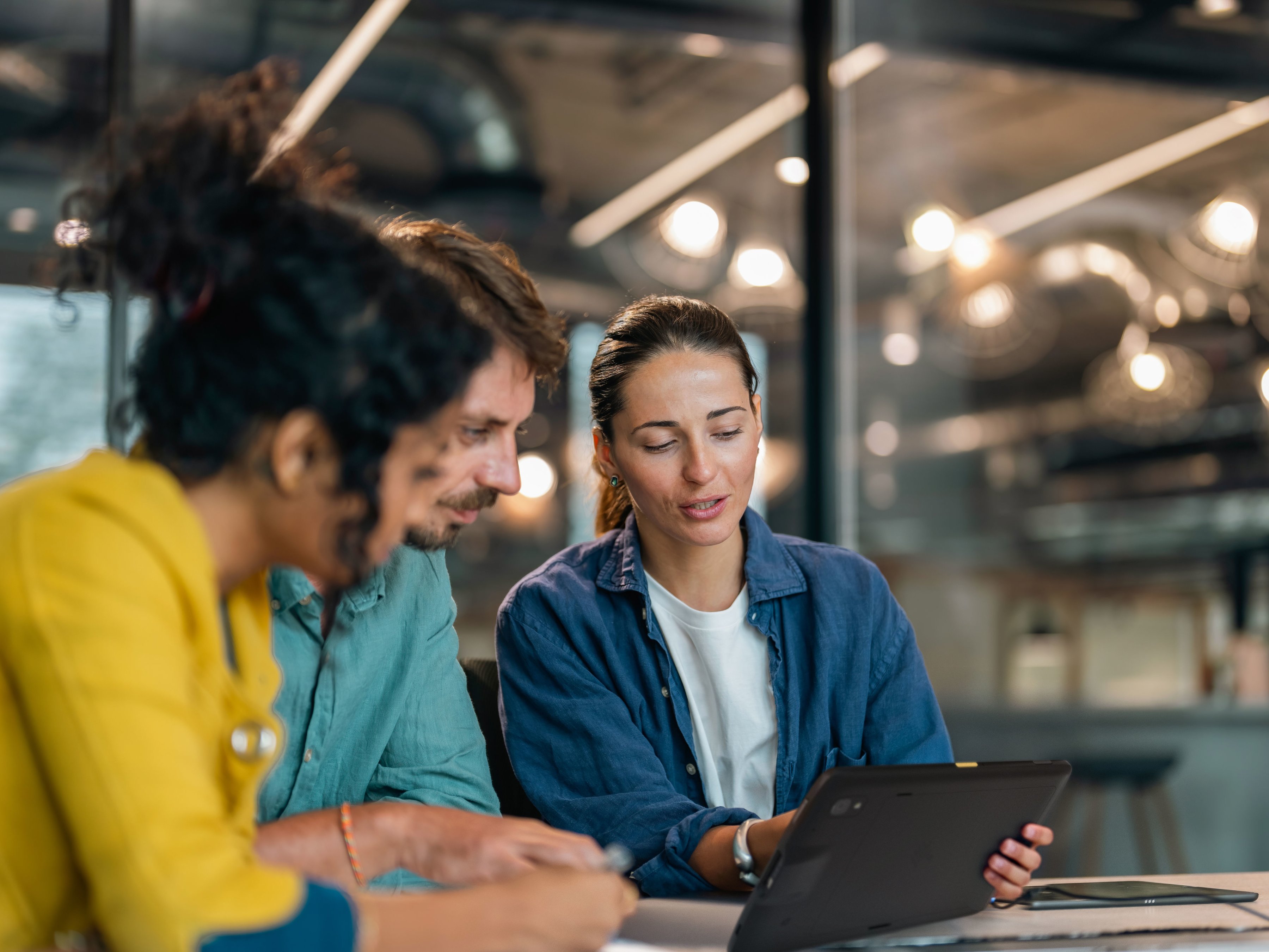 Three employees collaborating around a laptop during a meeting in a conference room.