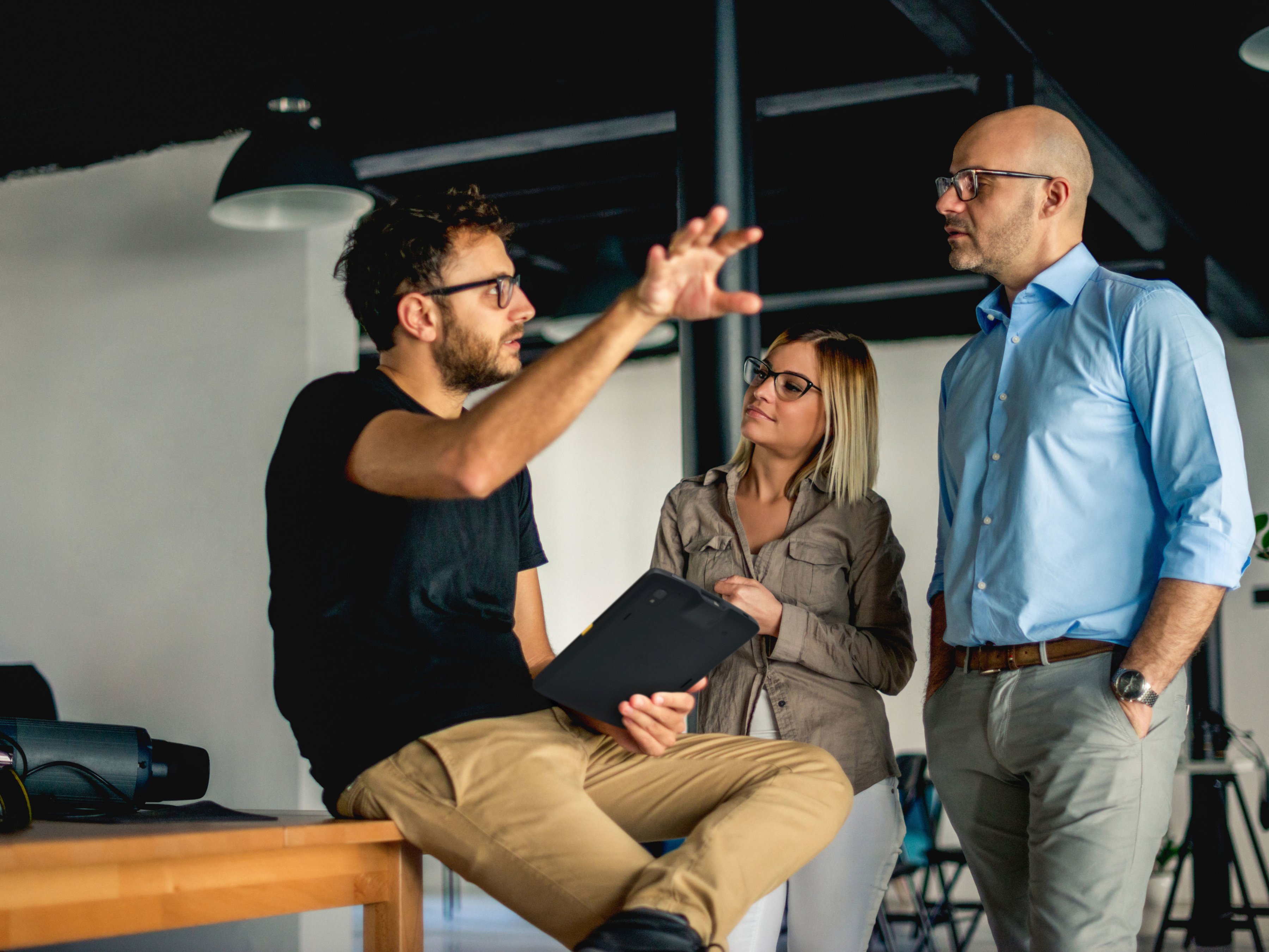 An employee with a tablet having a discussion with two colleagues inside of a modern office.