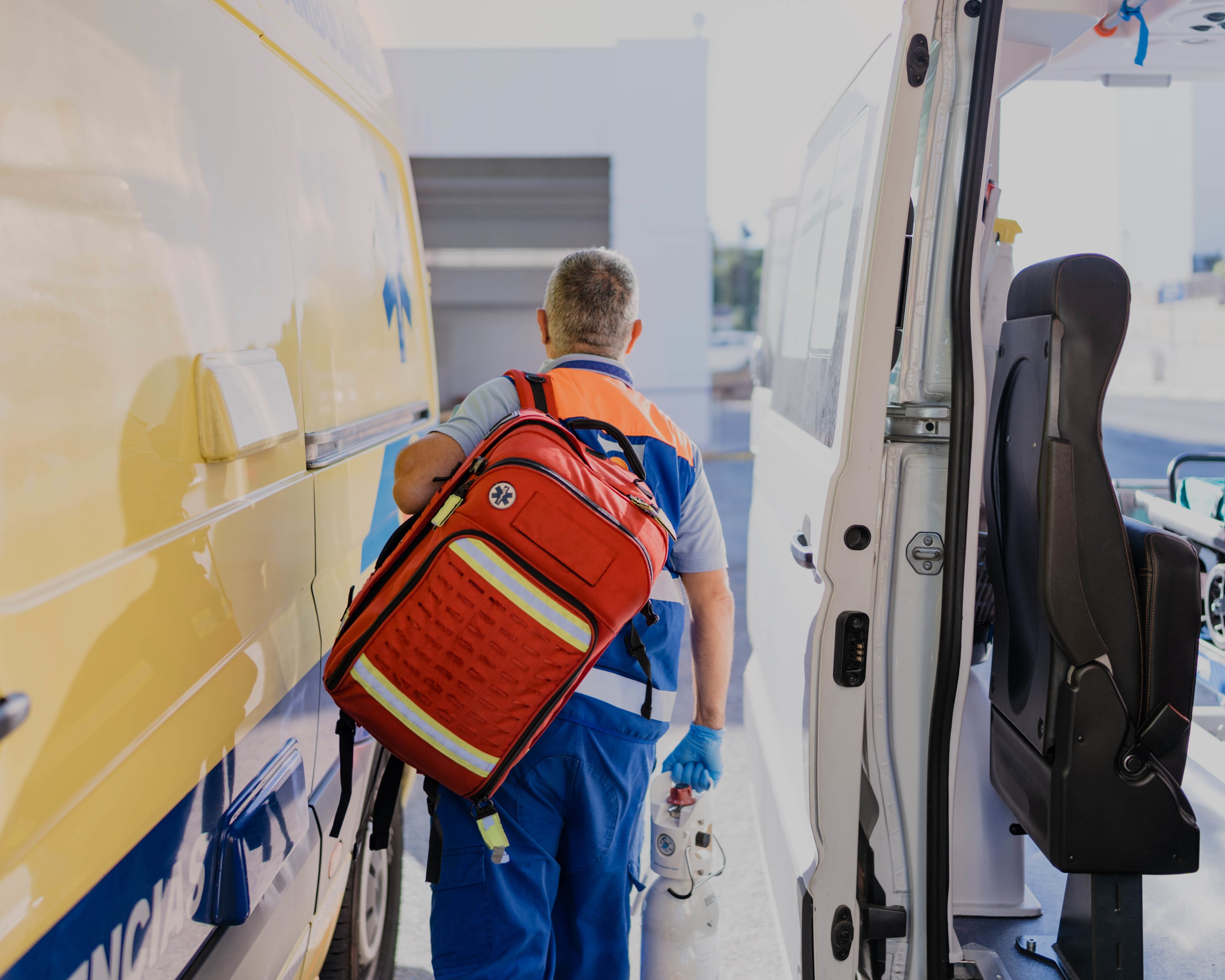 A paramedic walking between two emergency vehicles with a backpack on.
