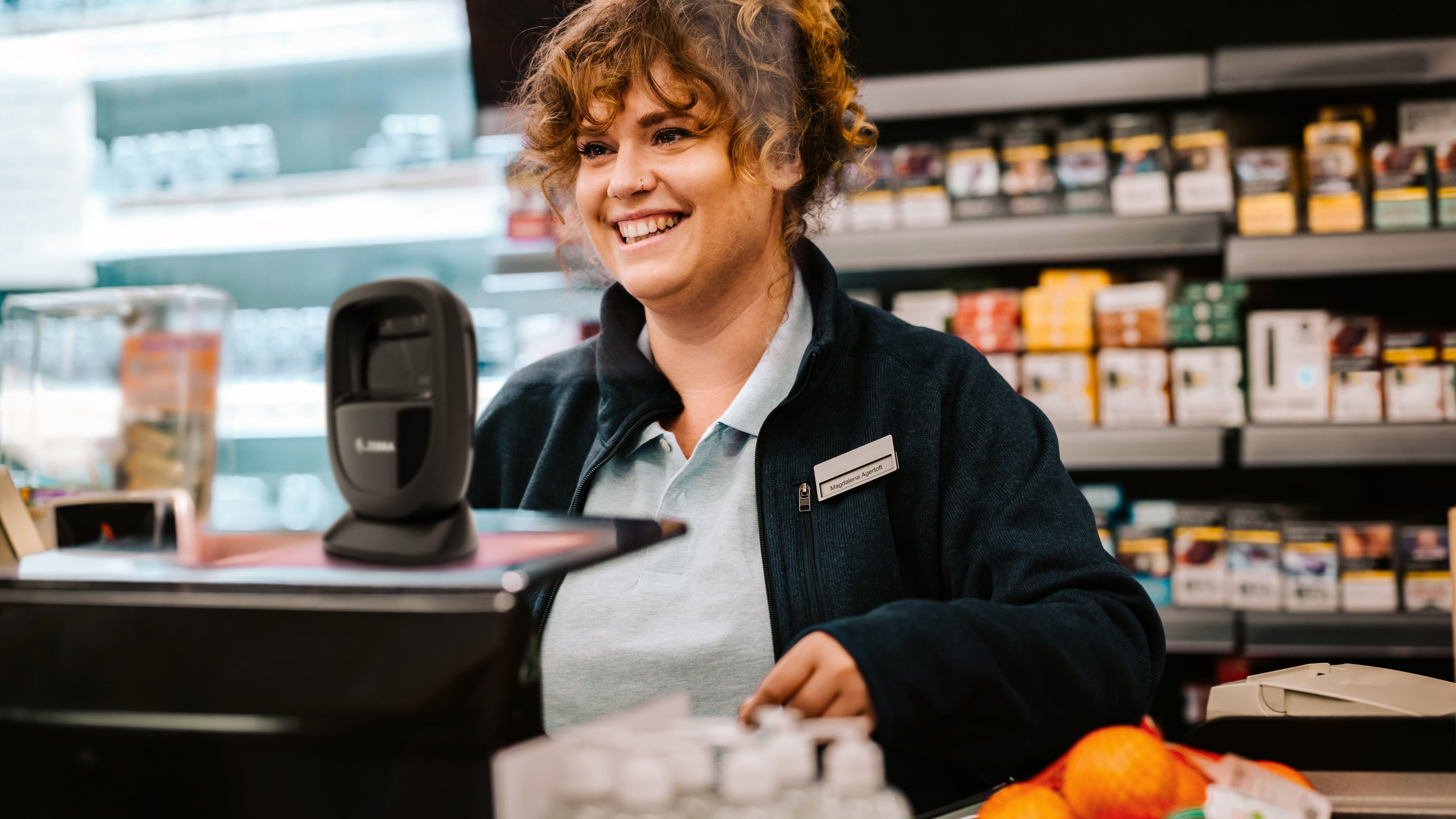 An employee smiling behind the checkout counter inside of a market.
