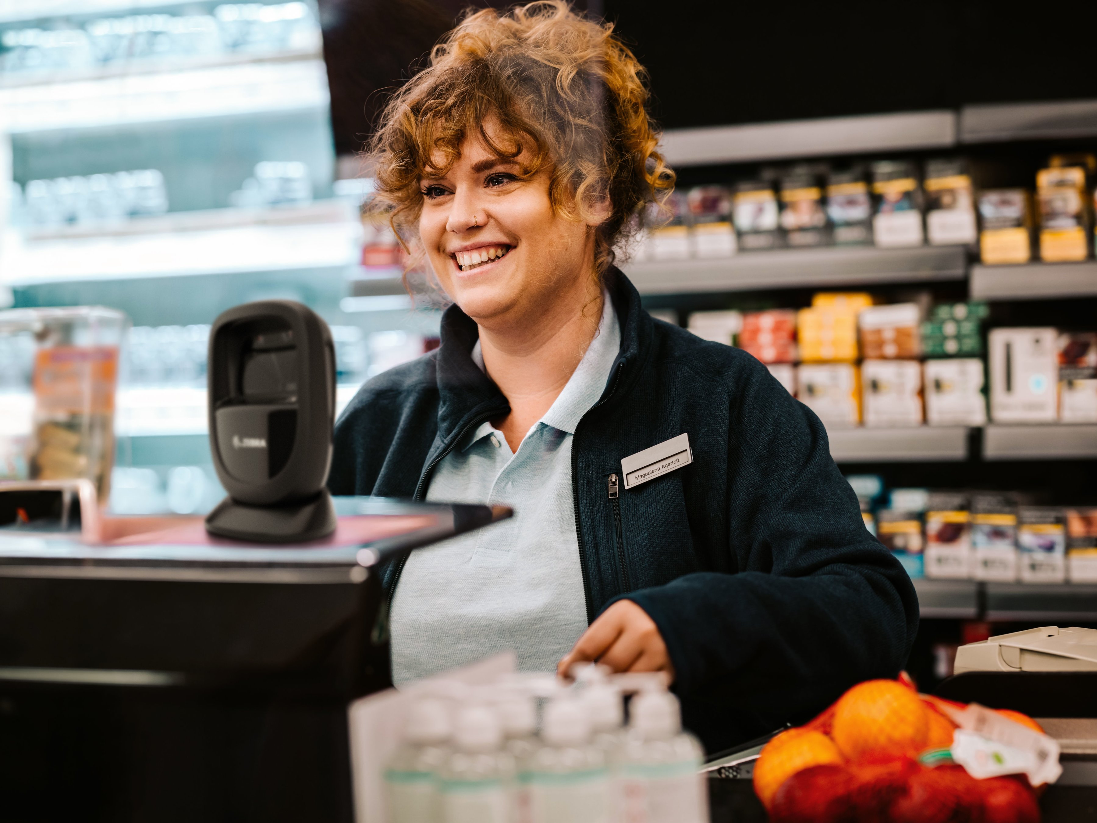 An employee smiling behind the checkout counter inside of a market.
