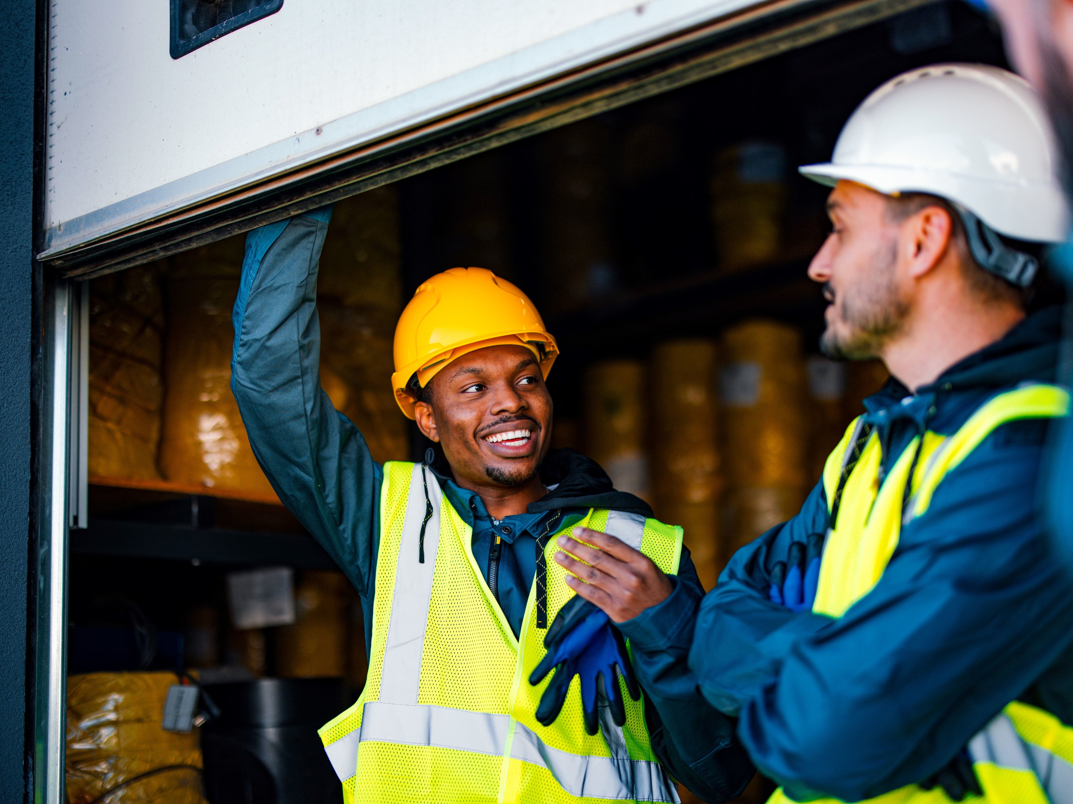 Two workers are standing in front of an open storage door, with one worker holding the door up and the other crossing arms while they talk.