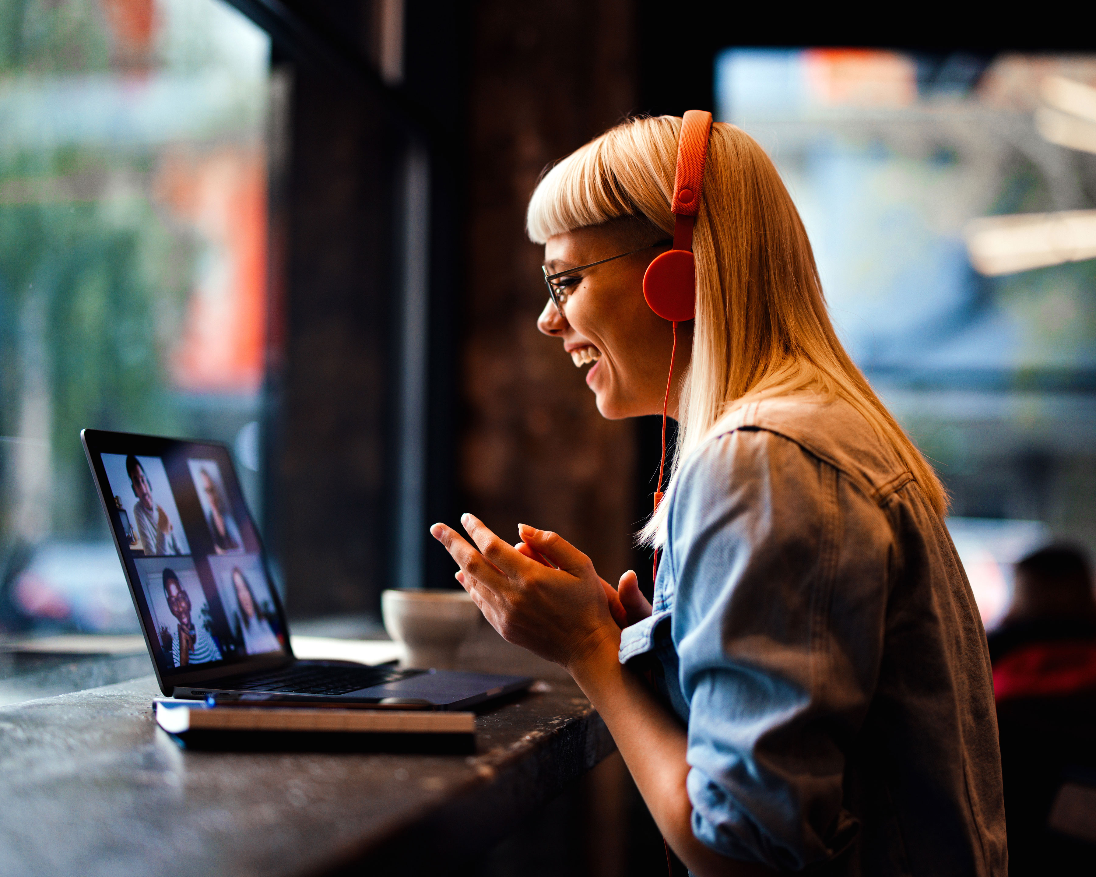 A worker using a laptop to take a conference call inside of a coffee shop.