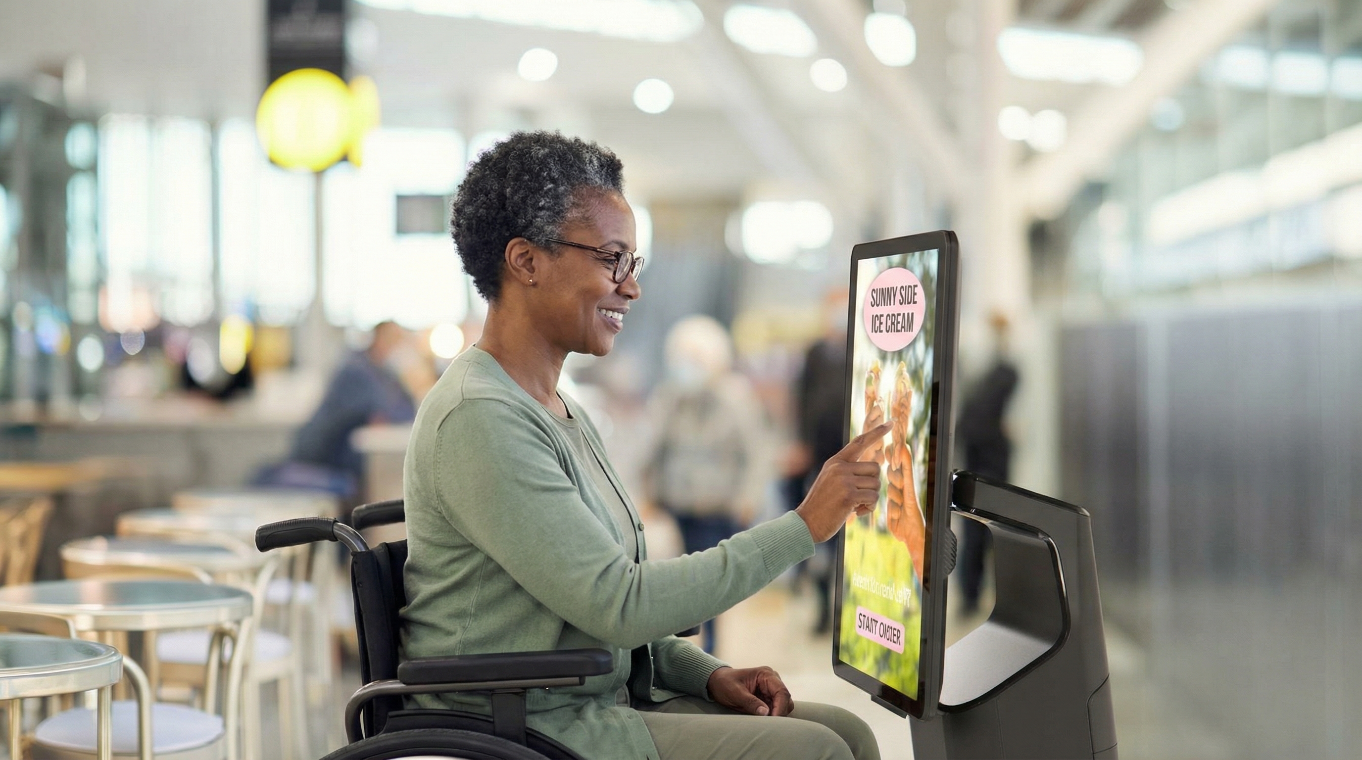 A wheelchair user uses a kiosk touchscreen to place an order.