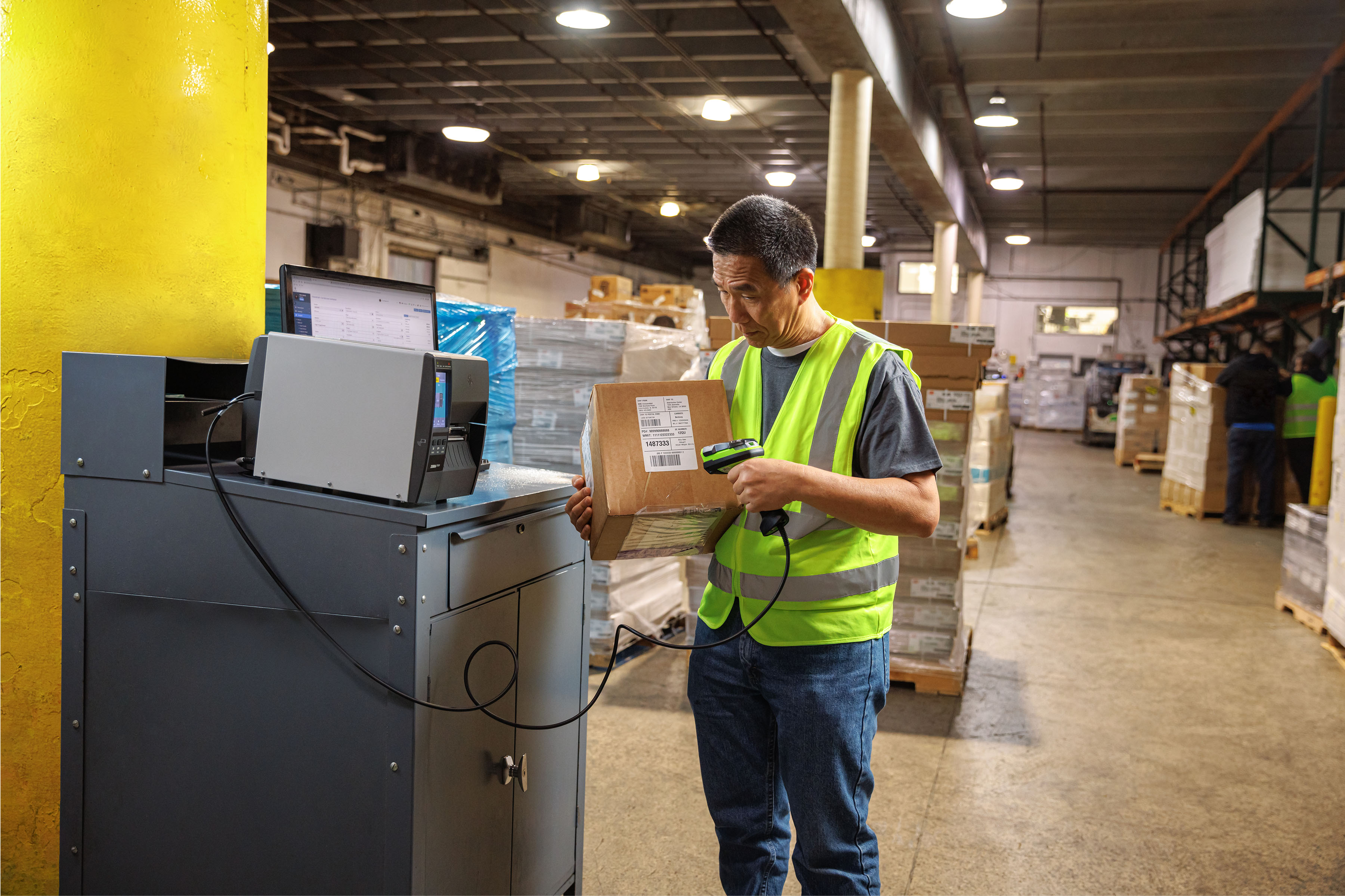 Man in a warehouse using a handheld scanner to read a barcode label on a box that he is holding. 