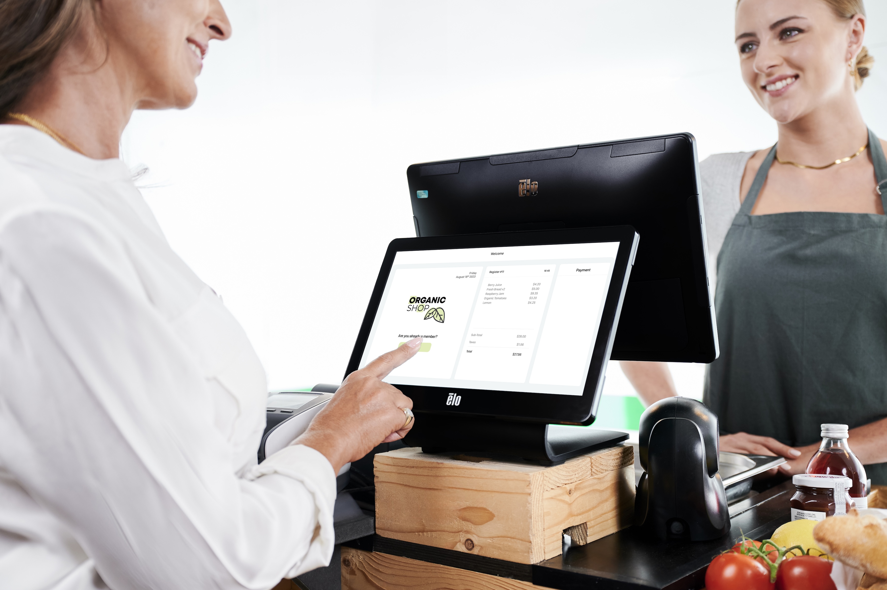 A customer interacts with an Elo touchscreen point-of-sale system during checkout while a store associate assists from behind the counter.