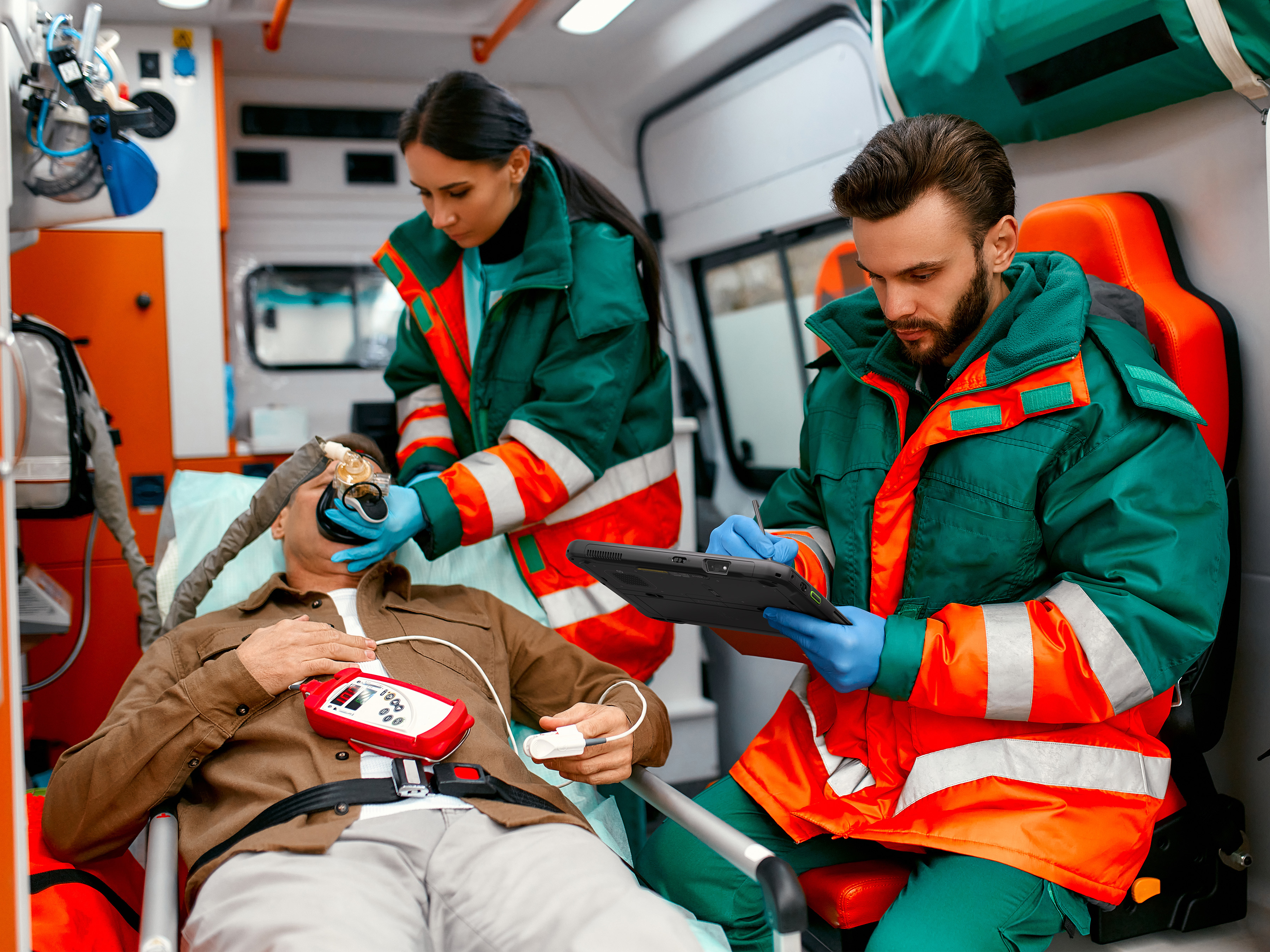 Two medics with a patient in the back of an ambulance with a patient. One EMT is making notes on an ET6 Series rugged tablet.