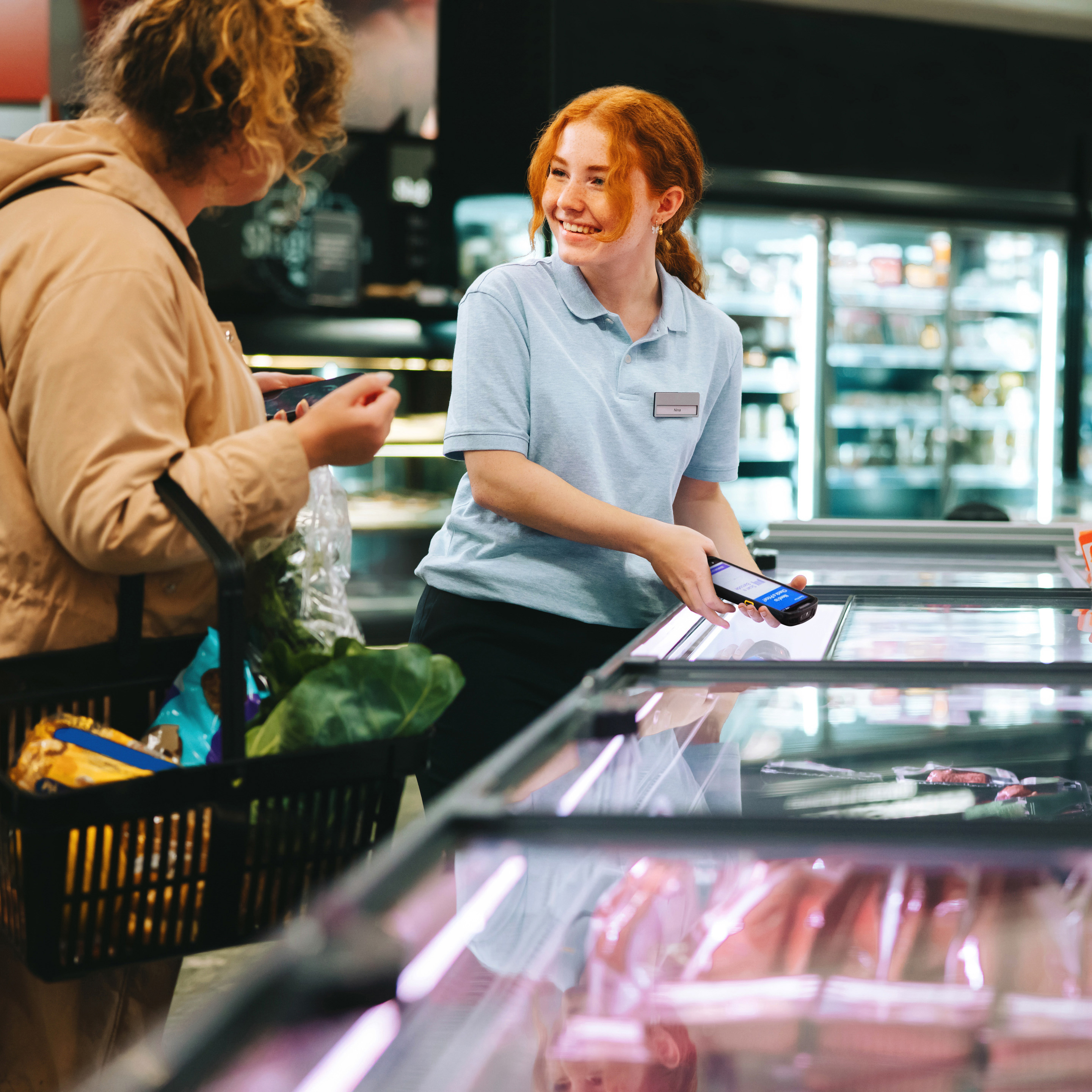 Retail employee with a Zebra handheld mobile computer assisting a customer in the meat department of a grocery store.