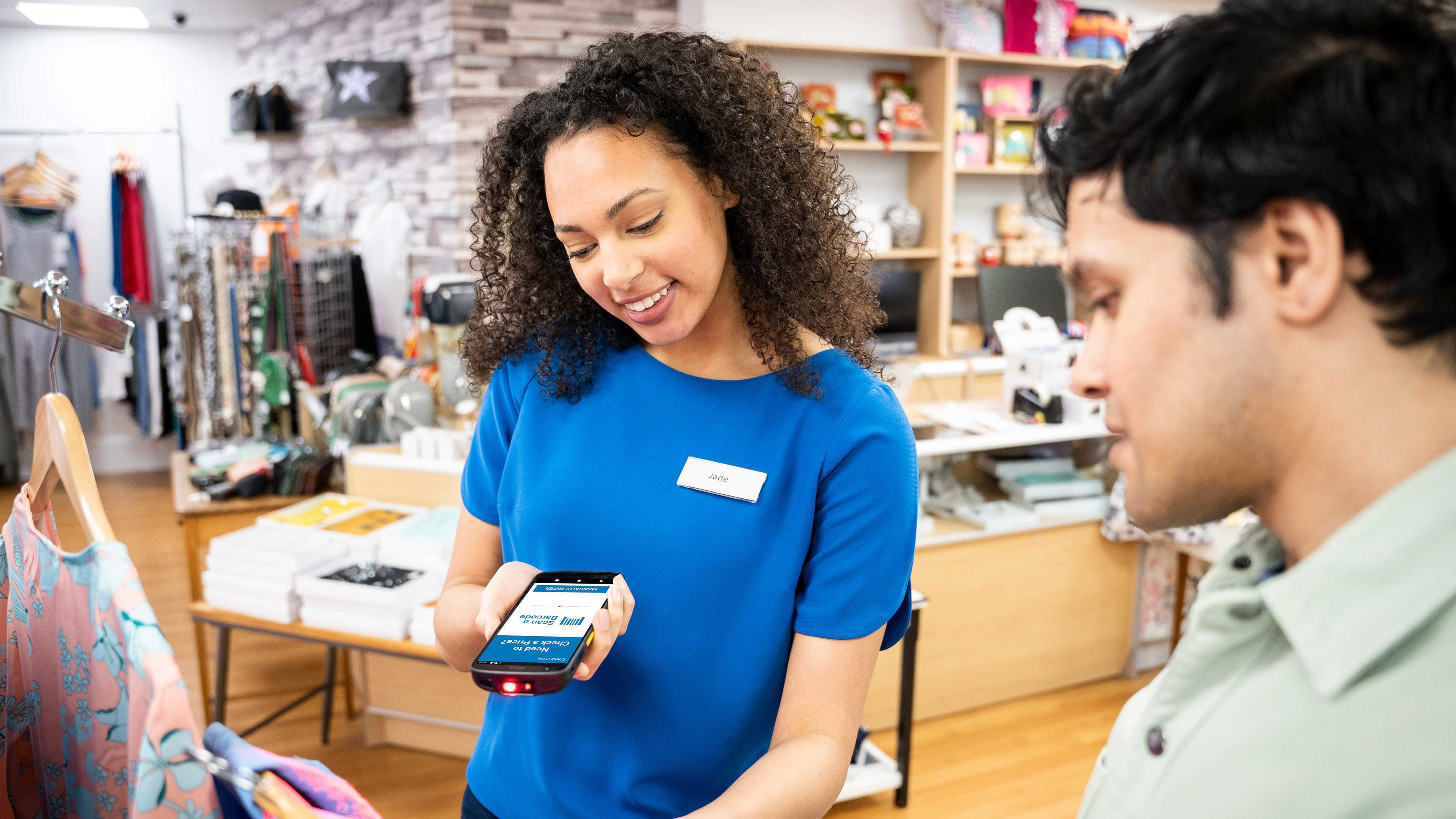 A retail associate uses a Zebra TC22 mobile computer to assist a customer with a price check in a clothing boutique.