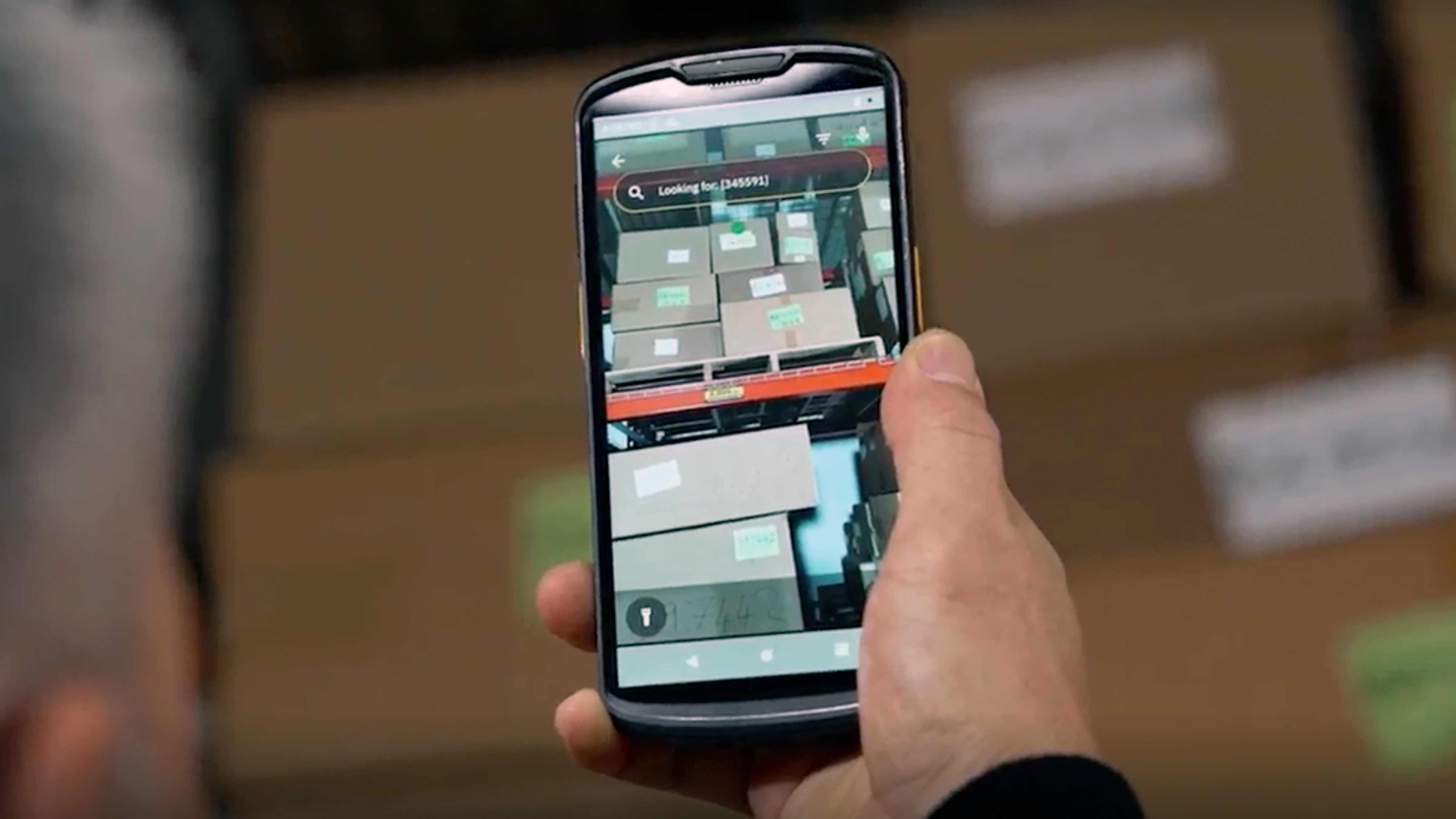 A warehouse associate  uses a Zebra TC701-series mobile computer  to run an augmented reality application that locates a specific package on a high shelf 