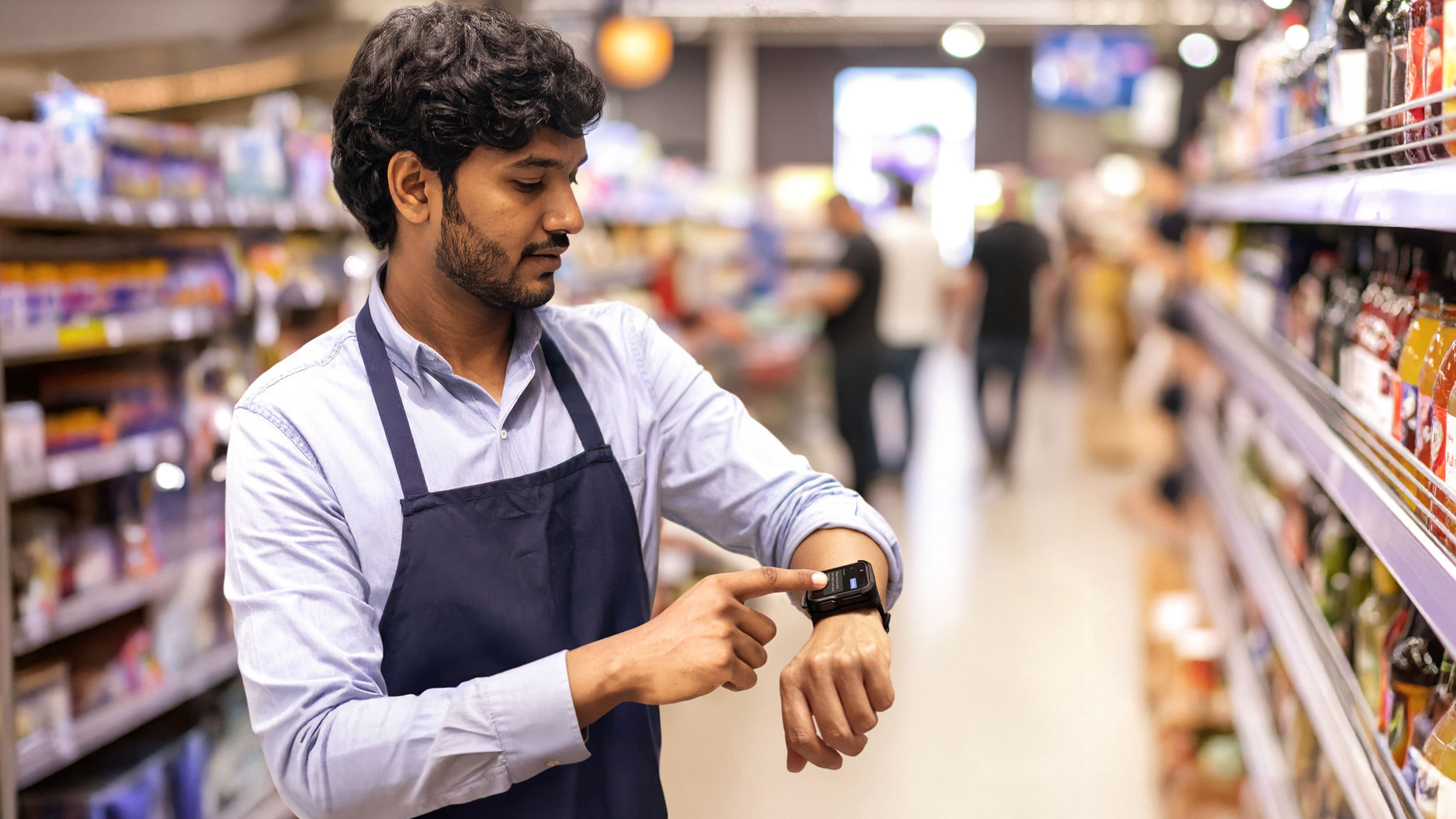 A retail grocery store employee uses a Zebra WS301 wrist wearable  on a grocery aisle