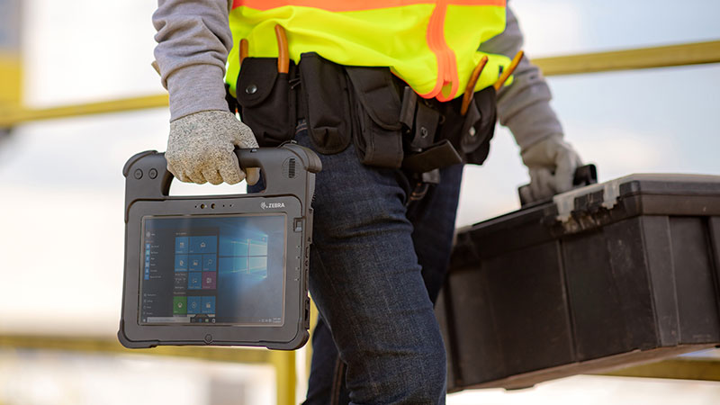 Funcionário da companhia de eletricidade carregando um tablet e uma caixa de ferramentas.