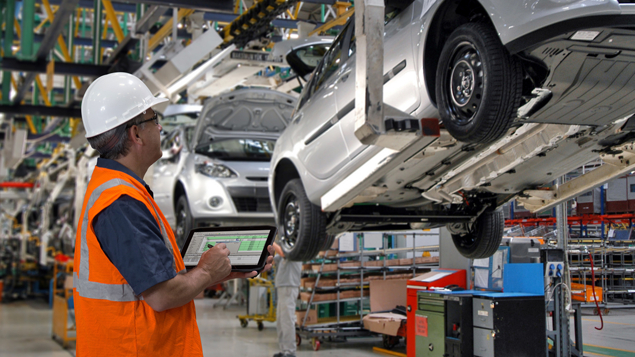 An automotive manufacturing assembly line worker uses a Zebra rugged tablet to take notes during a vehicle inspection.