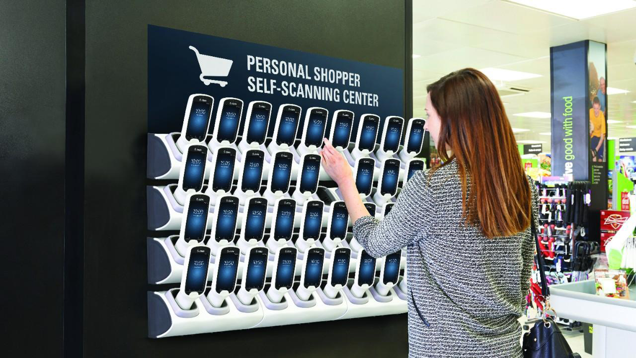 A woman grabs a smartphone from the Personal Shopping Solution display in a retail store.