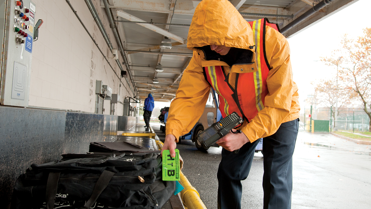 A baggage handler uses a handheld scanner to notate the location of a bag in transit to its next destination.