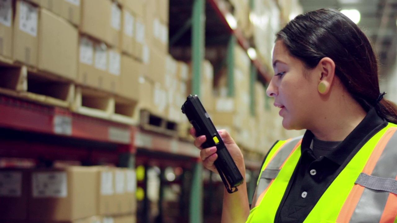 A warehouse worker uses a Zebra MC3300 mobile computer to communicate with a colleague