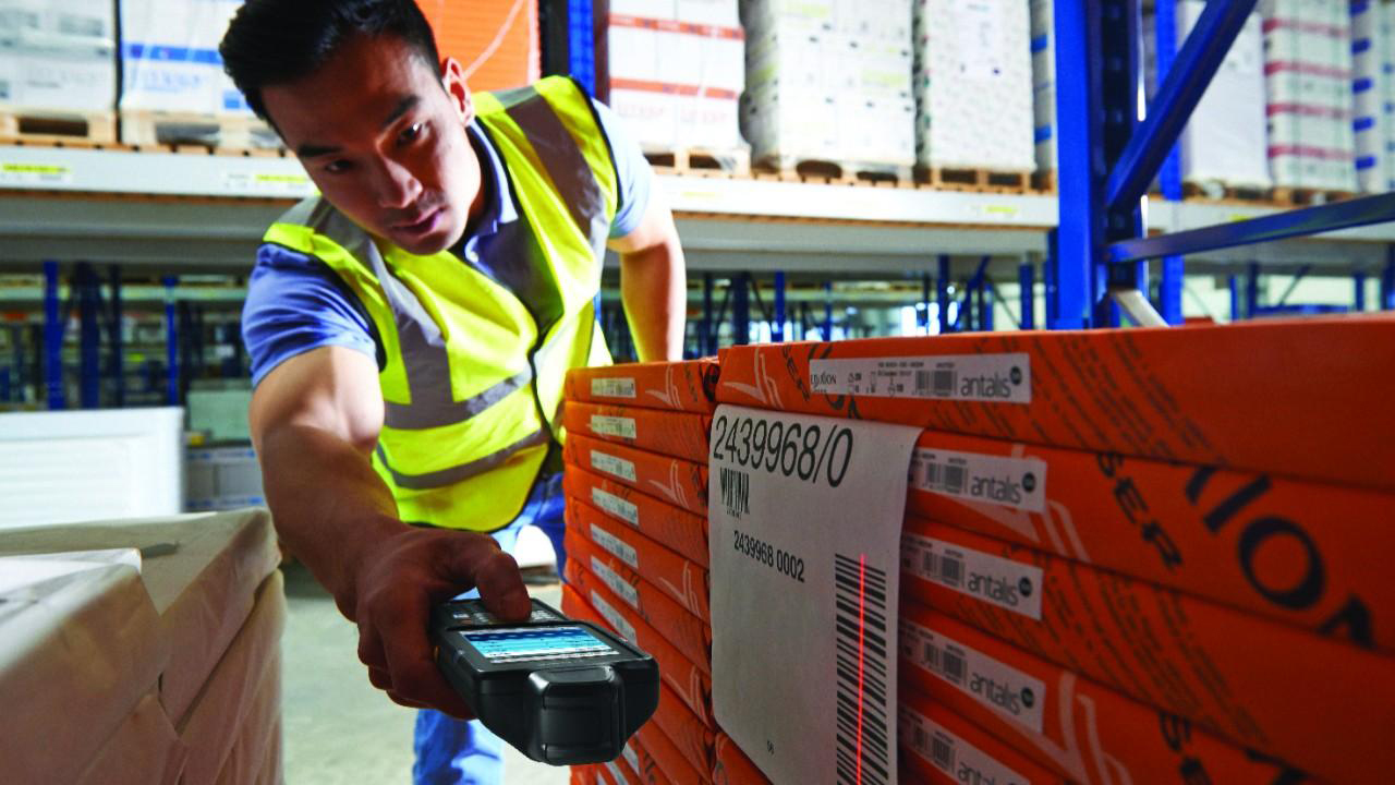 A warehouse worker uses an Android handheld mobile computer to scan the barcode on a pallet of products.