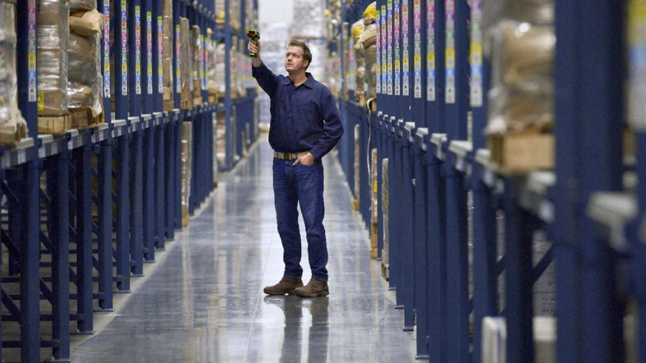 A male warehouse worker uses an extended range barcode scanner to capture information from inventory on high shelves