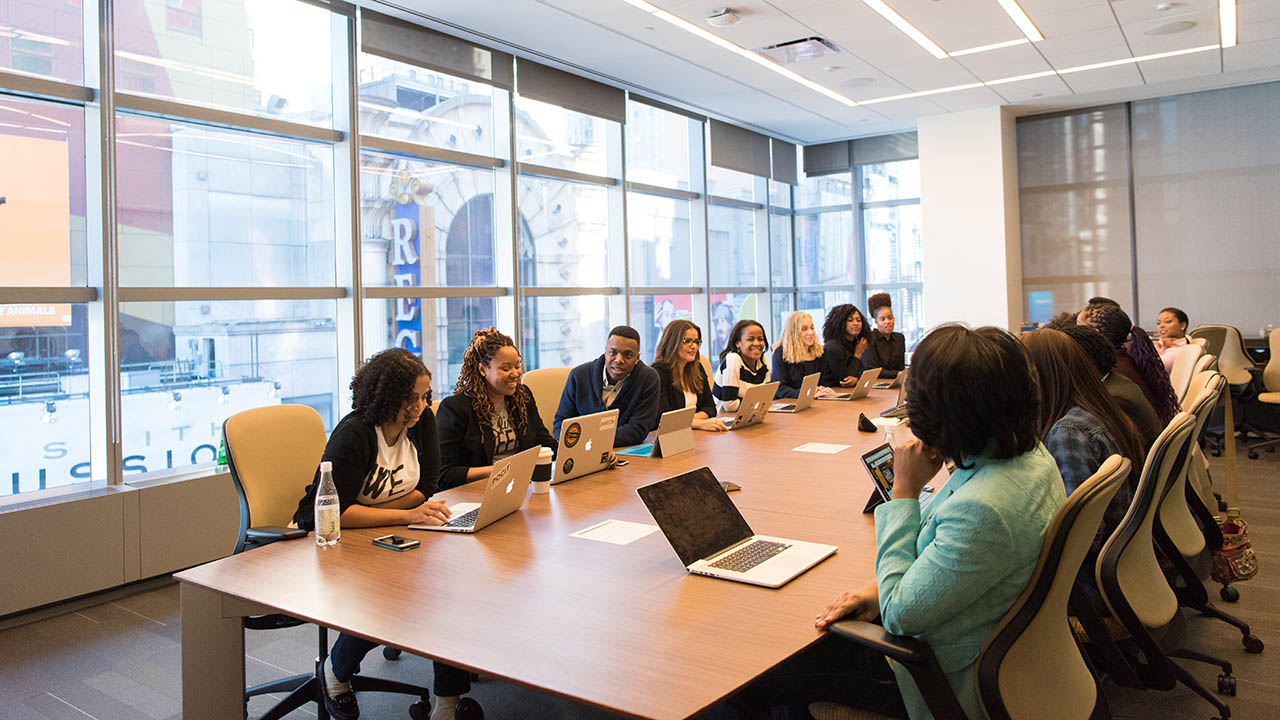 Several women sit at a conference room table discussing a project with their male colleagues