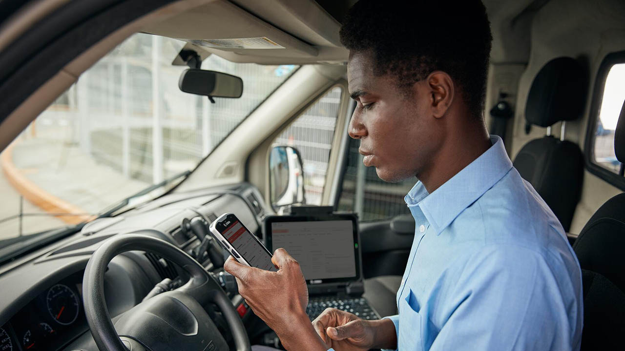 A utility worker looks at a handheld mobile computer in his truck