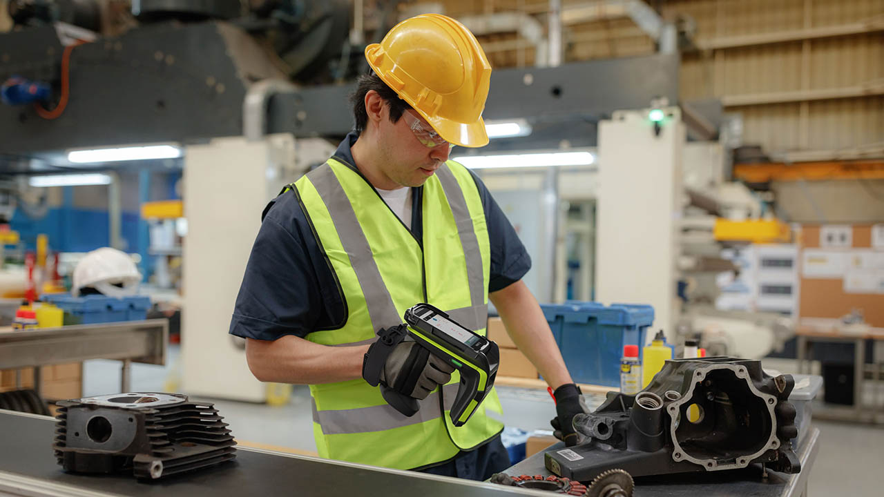 A factory worker uses a Zebra mobile computer equipped with an RFD90 RFID sled to read an RFID tag on a component