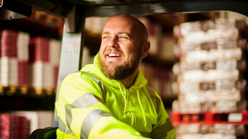 Smiling employee driving a forklift in a warehouse. 